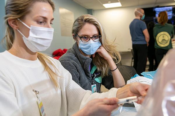 Two students wearing masks practice injections