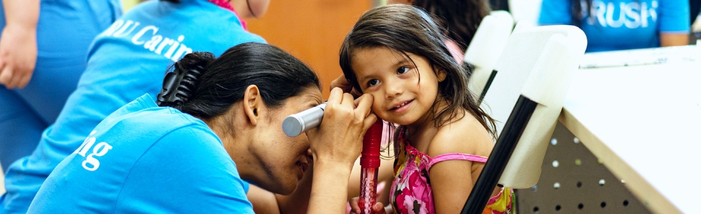 A RUSH student examining a little girl's ears through an otoscope