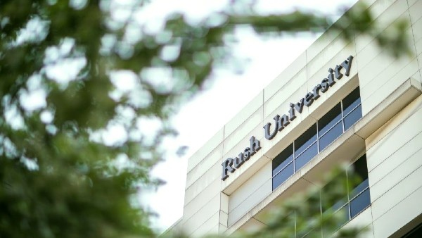 Signage on exterior building wall that reads RUSH University, with tree branches out of focus in the foreground