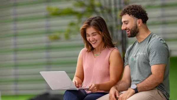 Two students seated outdoors looking at a laptop