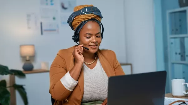 A woman seated in an office, facing a laptop and speaking into a headset microphone