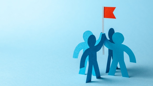 4 blue paper cutout people holding a red paper flag aloft