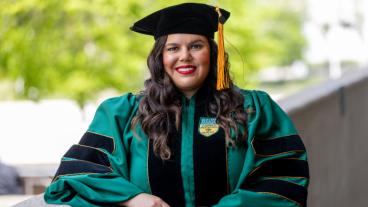 Delilah Flexas stands outdoors in full green and black commencement regalia.