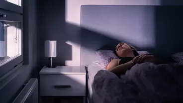 Woman sleeping in bed, with faint light streaming through the window