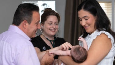 A mother and father hold a baby while a nurse listens to its chest with a stethoscope