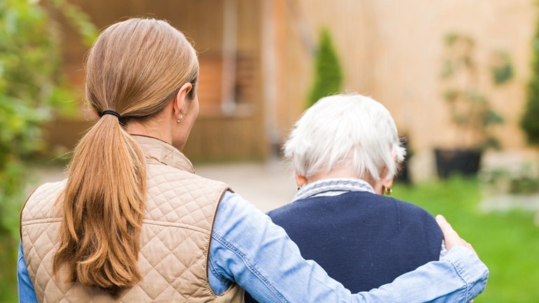 Younger woman with her arm around an older woman, seen from behind