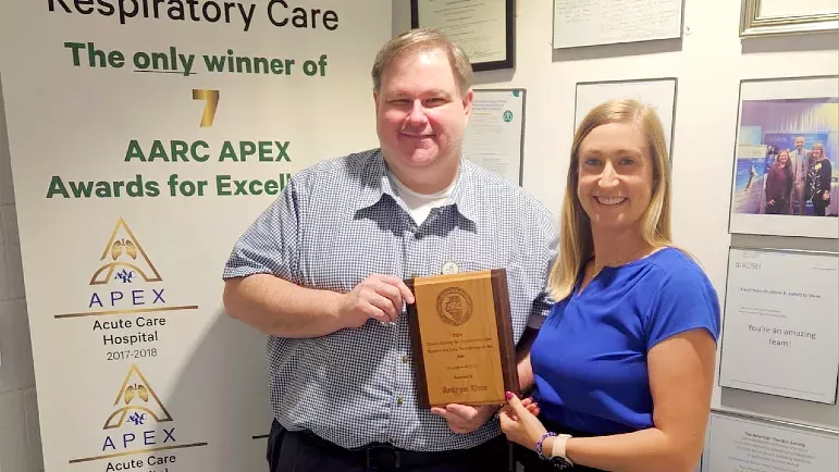 Two people stand together smiling and holding an award plaque